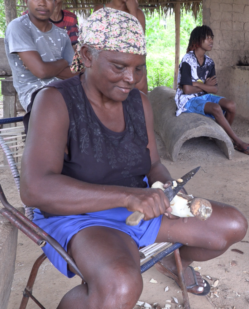 A woman sitting on the ground holding a knife and cutting Quilombola